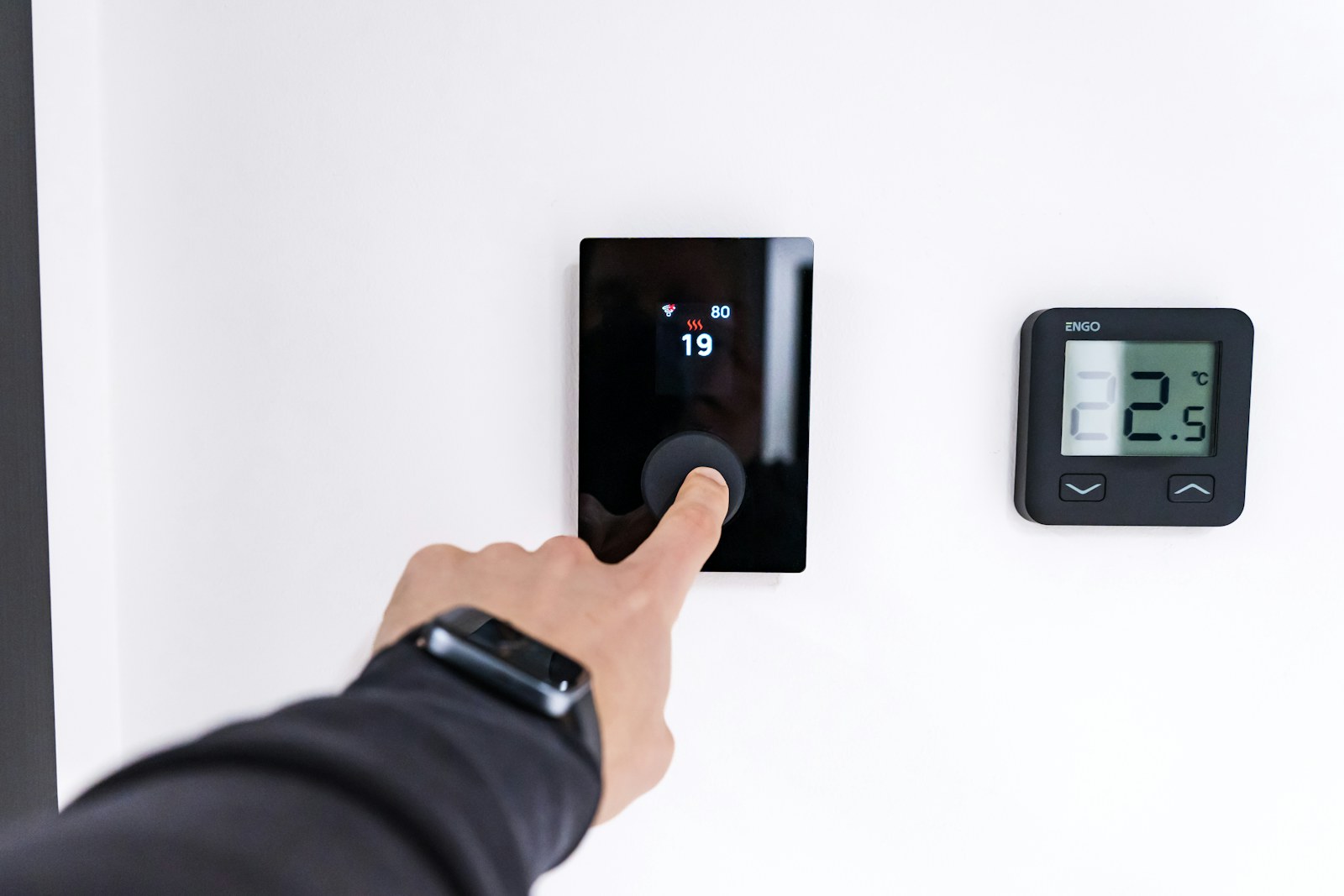 Hand adjusting a modern wall-mounted thermostat
